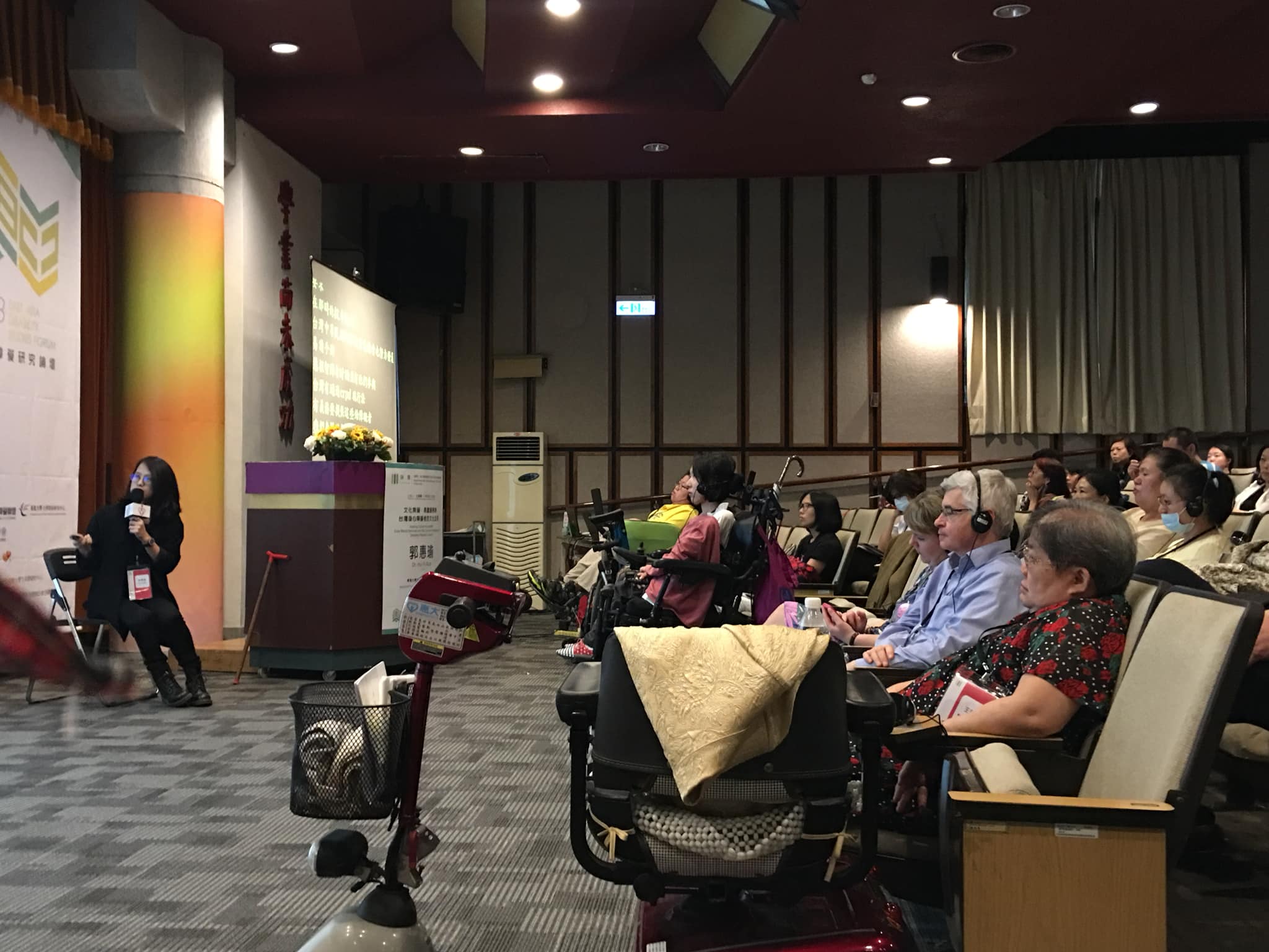 郭惠瑜在台前發表，側拍鏡頭捕捉到前排聽眾專心聽講的畫面，照片前景有一台代步車